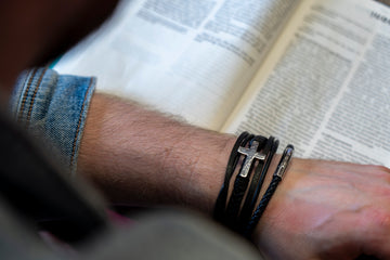 a man is holding a book and wearing a cross bracelet